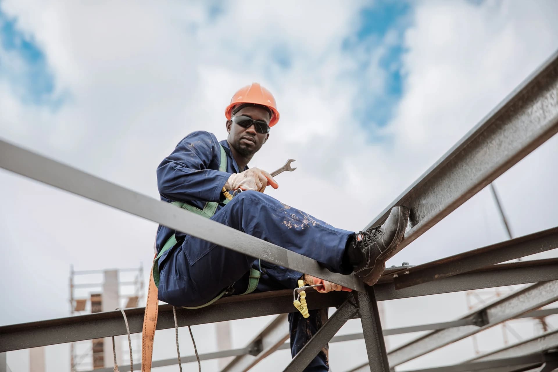 Worker in a hard hat, safety harness, and protective workwear secured on a steel structure
