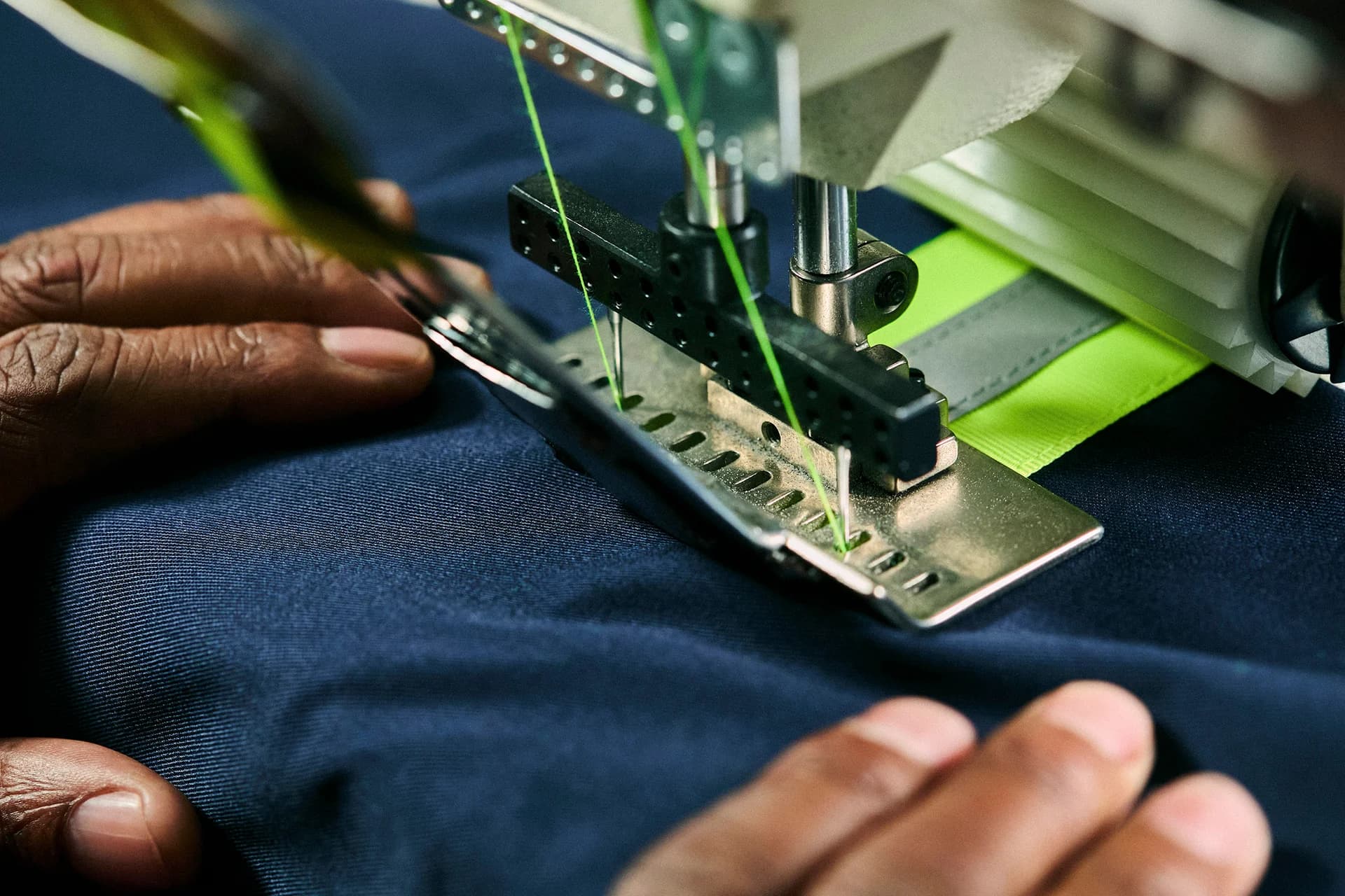 Close-up of an industrial sewing machine stitching reflective tape onto workwear fabric
